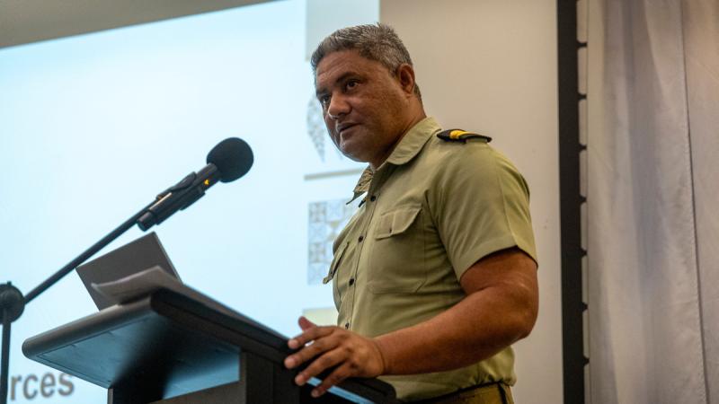 A man in uniform delivers a presentation at a podium.