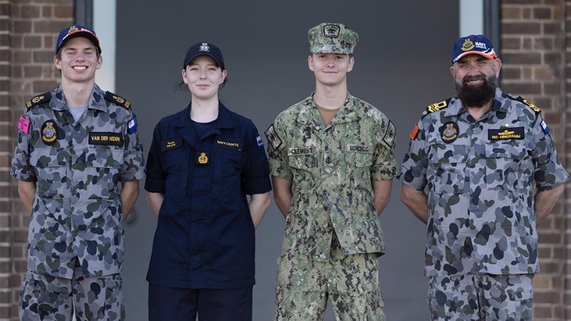 Three teenagers and a man in military uniforms standing side by side.