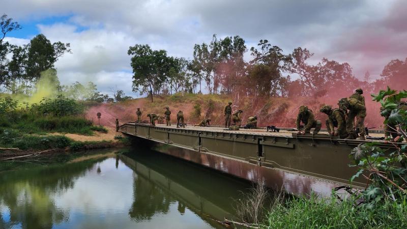 Soldiers work in a bridge while pink smoke floats in the background.